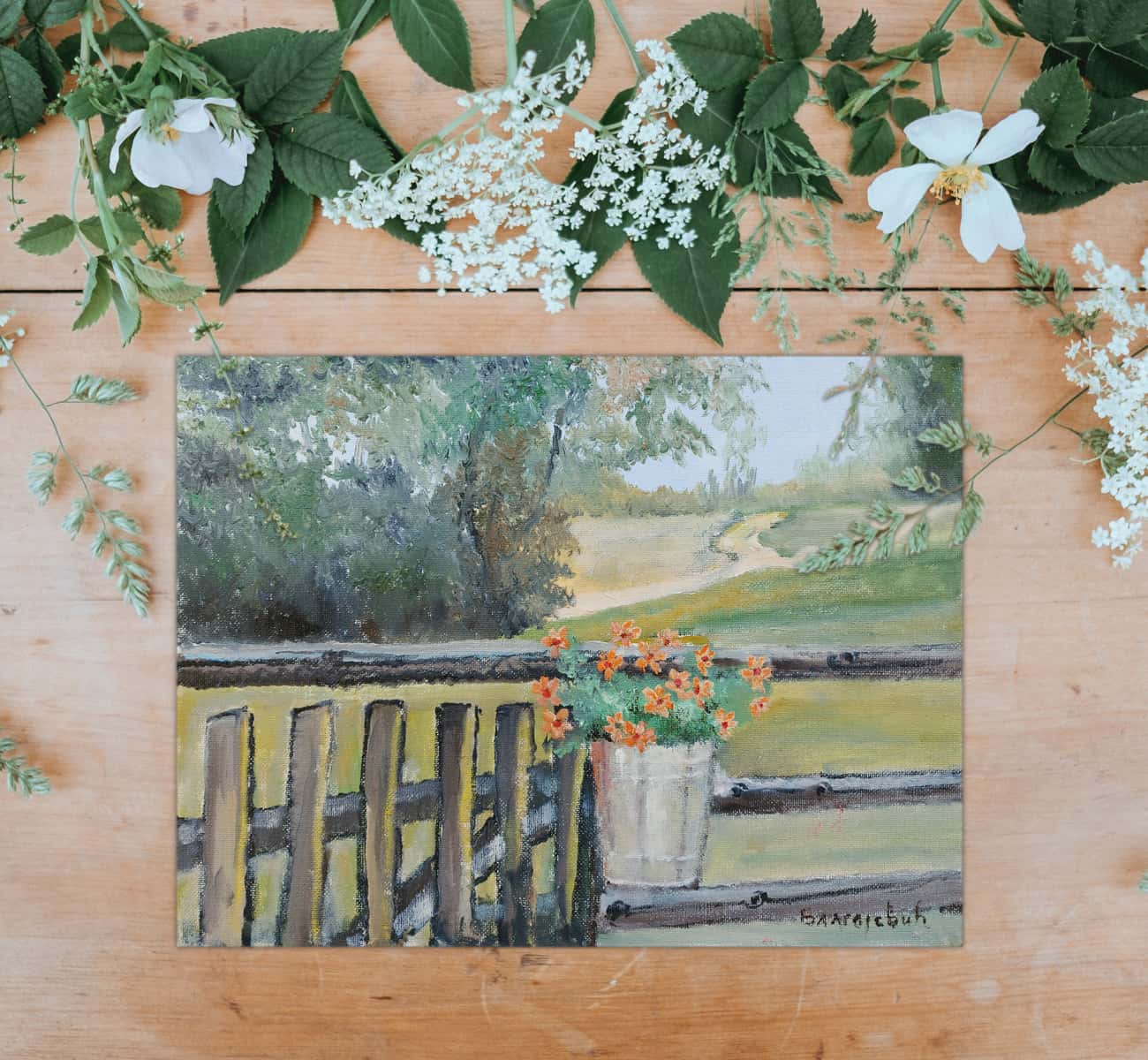 Greeting card depicting country flowers in a bucket hung on the country fence laid on top of the dried stems with tiny white flowers.