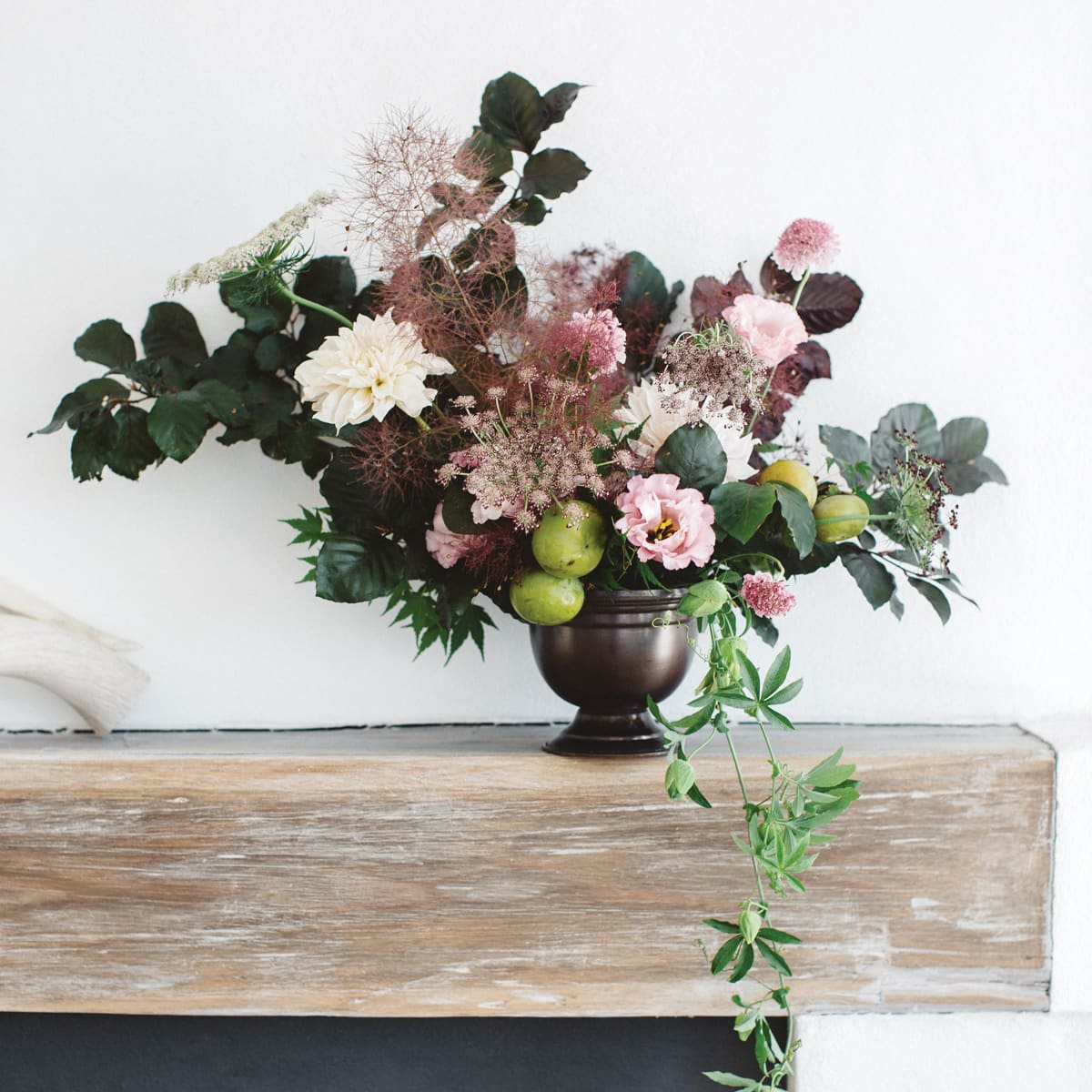 A large moody compote floral arrangement on the modern fireplace mantel announces the farm fresh florist product category.