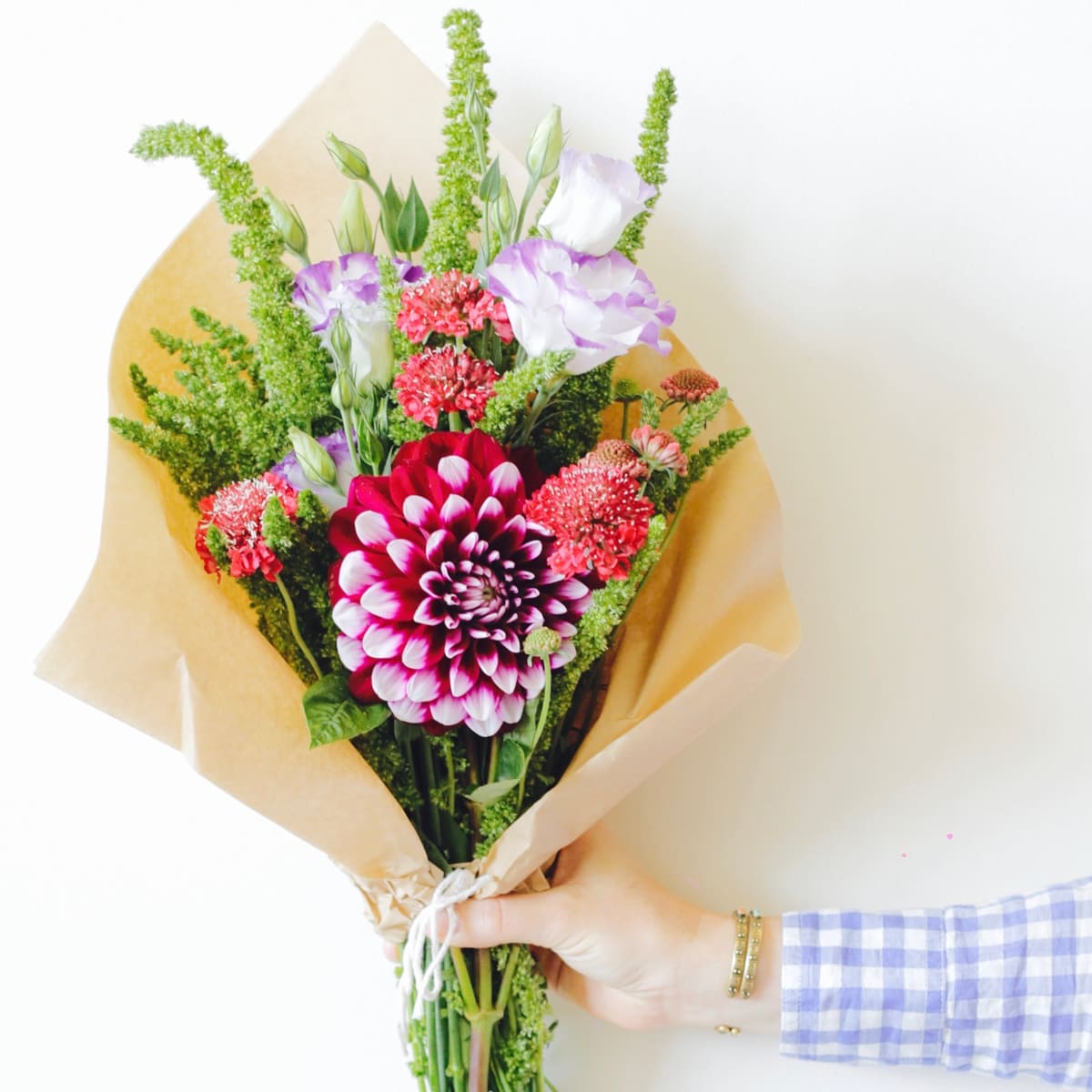 A hand holding a paper-wrapped colourful bouquet announces the flower subscription product category.