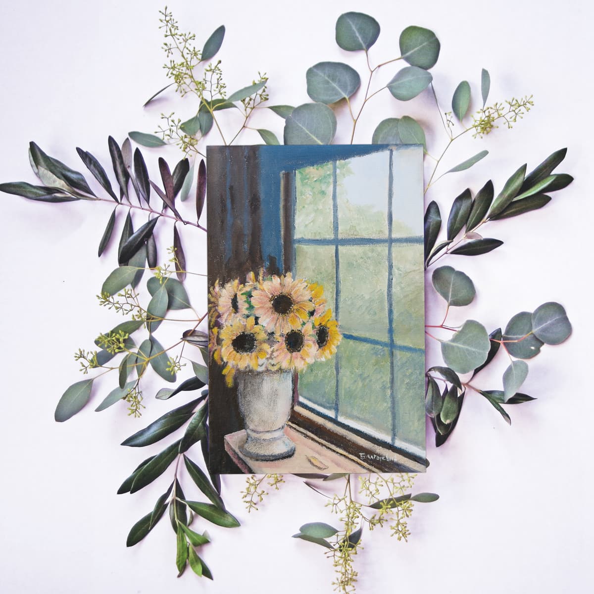 A greeting card with a sunflowers painting laid against the eucalyptus branches announces the greeting card product category.
