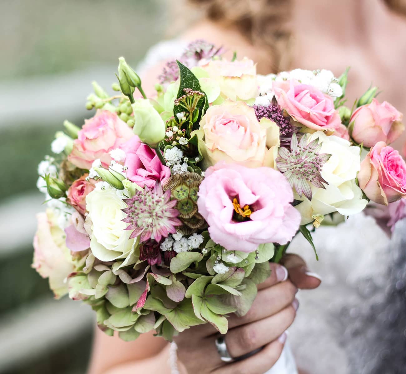 A lush pink bridal bouquet held by a bride represents what comes as a part of wedding flower packages.
