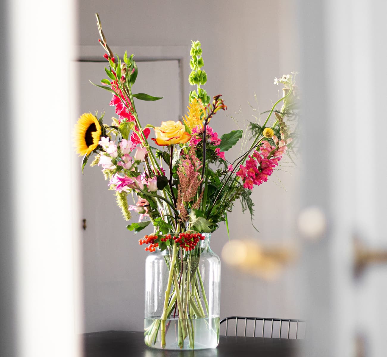 A big glass vase in a bright space holds a colourful DIY flower arrangement.